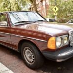 Front three-quarter view of a red Mercedes-Benz 240D parked on a paved area, showcasing its classic sedan design