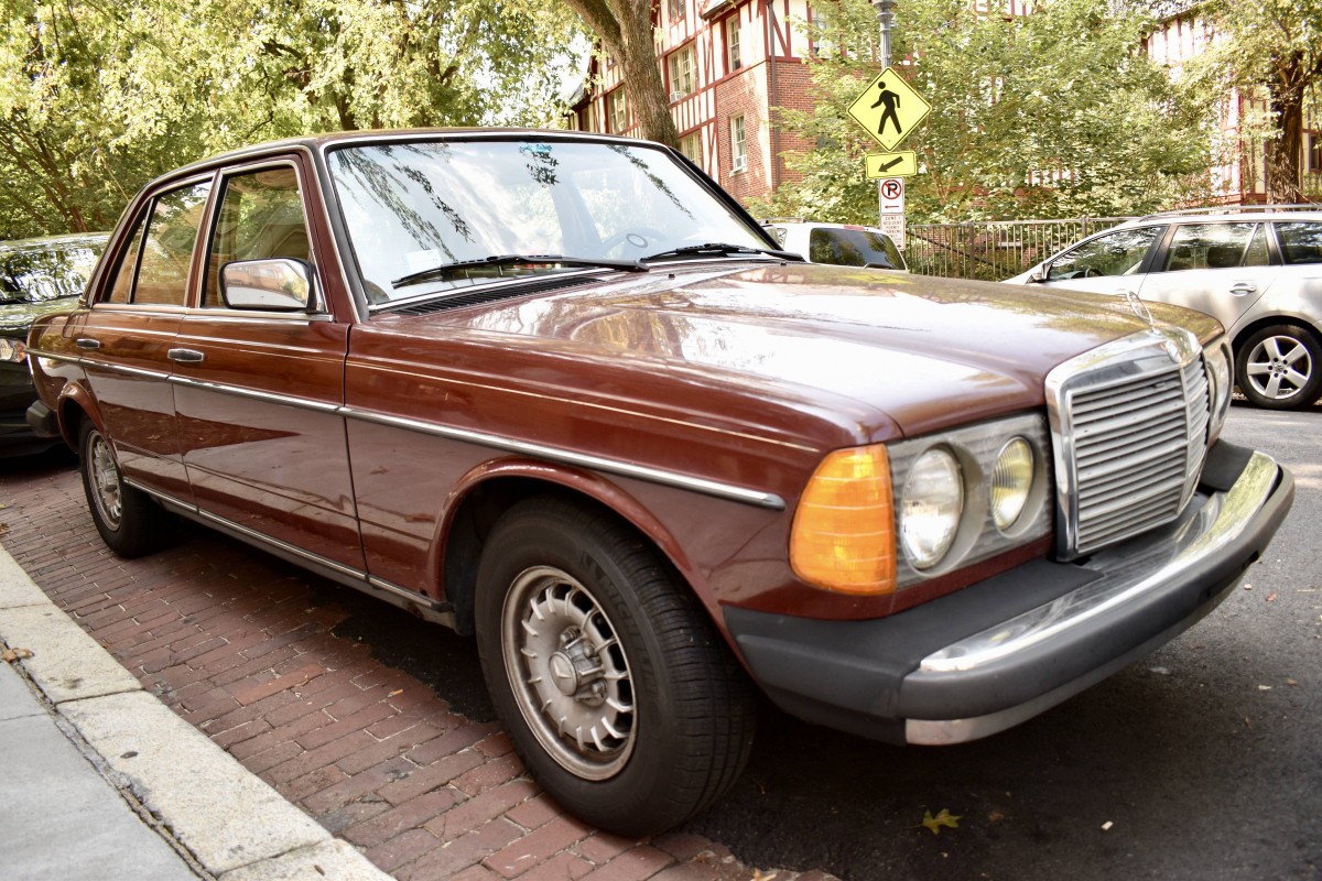 Front three-quarter view of a red Mercedes-Benz 240D parked on a paved area, showcasing its classic sedan design