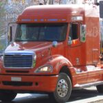 An orange Freightliner Columbia truck towing a load of logs