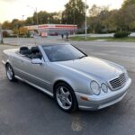 Front quarter view of a silver Mercedes-Benz CLK 430 convertible with the top up, parked on a paved surface showcasing its elegant design.