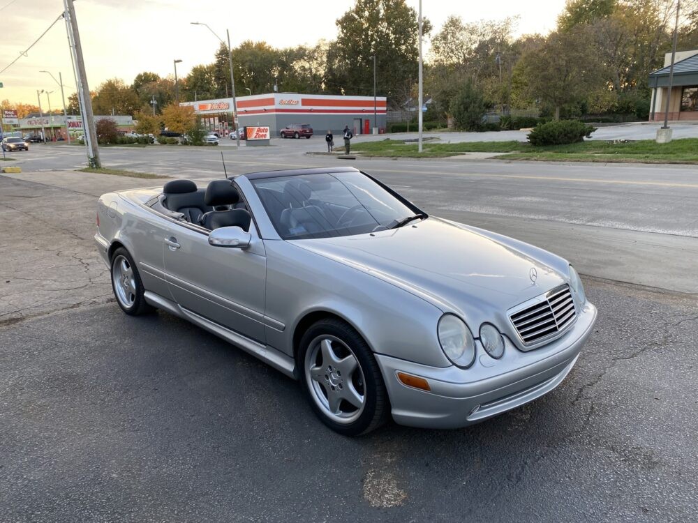 Front quarter view of a silver Mercedes-Benz CLK 430 convertible with the top up, parked on a paved surface showcasing its elegant design.