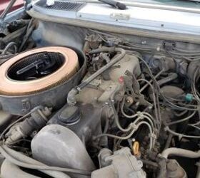 Front view of a dusty 1985 Mercedes-Benz 300D in a junkyard, highlighting its classic W123 body shape and round headlights, showcasing its age and condition as a junkyard find.