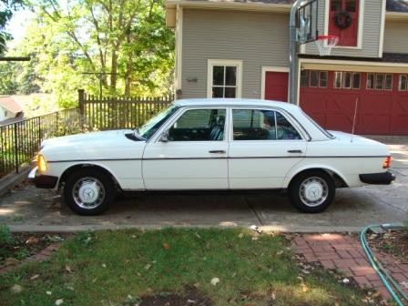 Front quarter view of a white Mercedes Benz 240D parked on a paved surface, showcasing its classic boxy design and iconic Mercedes grille.