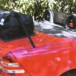 red Mercedes slk r170 next to a bush in shine under shade with a boot-bag trunk luggage rack fitted