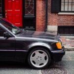 Front three quarter view of a black Mercedes-Benz 500E showing its wider stance and flared fenders.